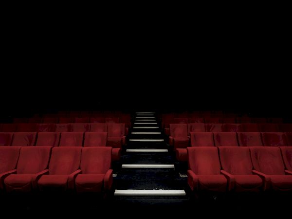 A dimly lit empty movie theater with red seats and a center aisle leading to a dark screen, quiet and ready for an audience.