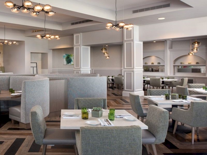 A modern, airy restaurant with gray booths, round tables, and soft lighting; wood-pattern flooring and stylish ceiling fixtures. (ends with period)